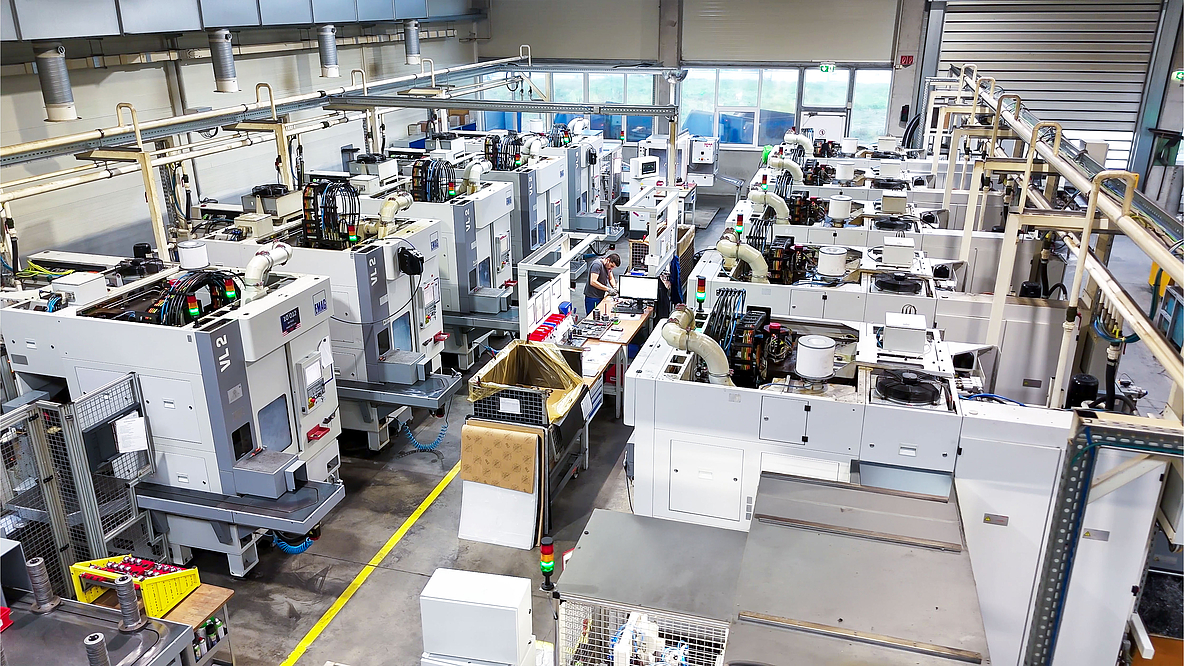 Bird's eye view of a large production hall with numerous white EMAG lathes in rows, demonstrating the extensive production capacity of PENN GmbH with a total of 43 spindles.