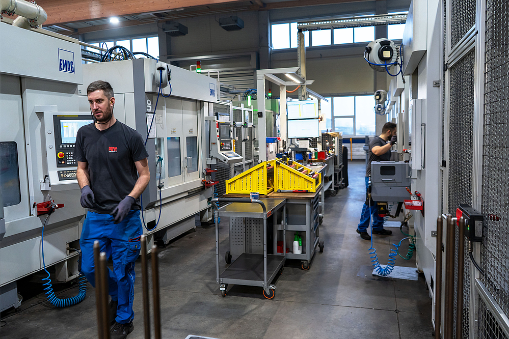 Production hall with EMAG VL 3 DUO and VL 2 lathes, connected by a TrackMotion system, with an employee in the foreground monitoring the automated machining of automotive parts.