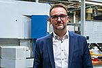 Portrait of Gernot Penn, Managing Director of PENN GmbH, in a blue suit with white shirt and glasses, standing in the company's production hall.