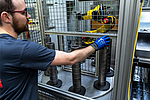 Skilled worker with blue gloves operates workpieces on an automated EMAG VL 2 manufacturing cell with robot technology behind safety fences.