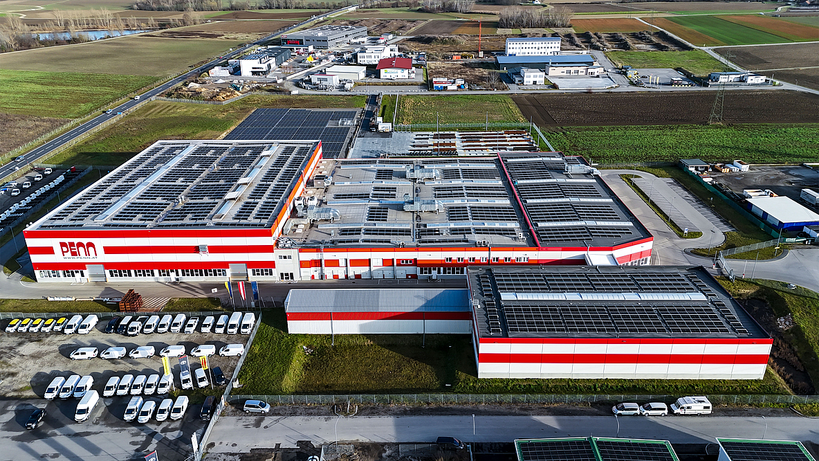 Aerial view of the PENN GmbH industrial complex in Stratzdorf with several modern production buildings and red and white façade elements, surrounded by parking lots and agricultural land.
