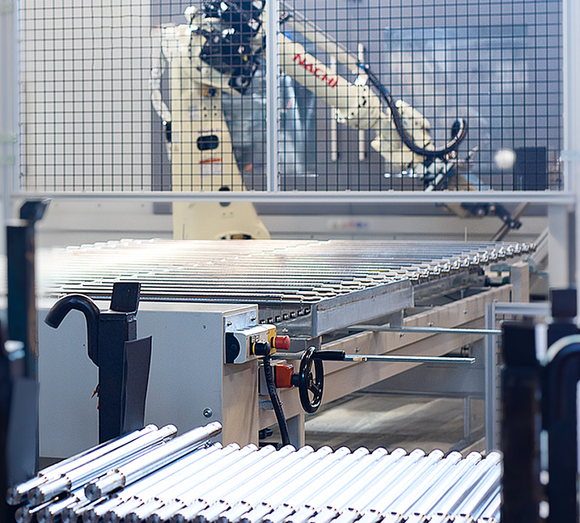 Roboter automatisiert die Beladung und Handhabung langer Antriebswellen an einer Werkzeugmaschine.